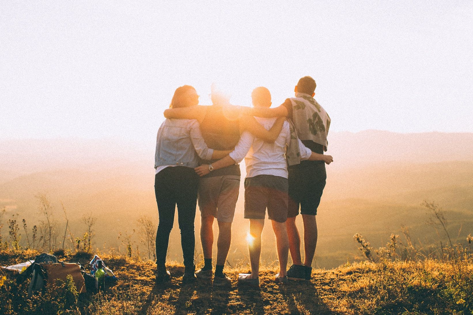 positiv bild av 4 ungdomar som står tillsammans, håller om varandra och tittar mot horisonten och solnedgången